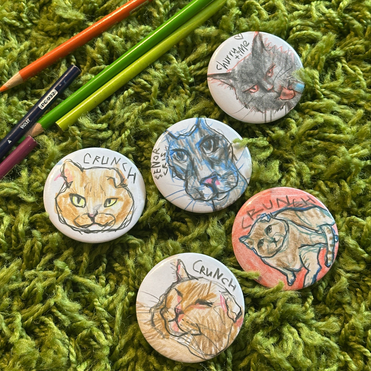 Five custom cat portrait buttons featuring colorful hand-drawn illustrations beside colored pencils