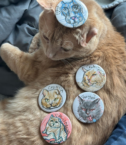 Orange tabby cat resting with five hand-drawn cat portrait buttons arranged on its fur