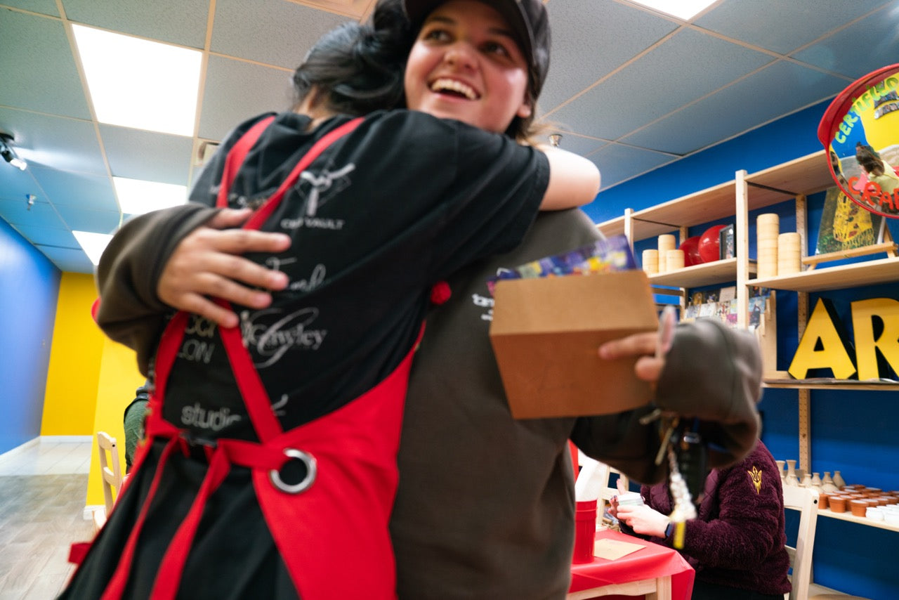 Person hugging Crafty Tomato owner in a red apron with a colorful background